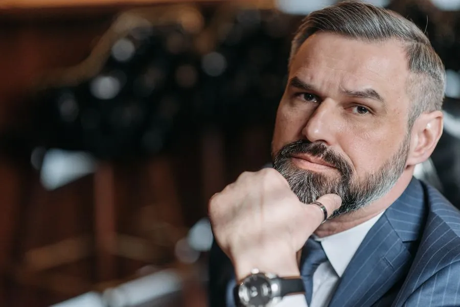 An older man with a grey beard in a dark suit